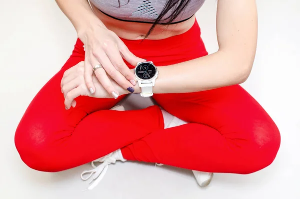 女の子 赤いスポーツ レギンスで胡坐フィットネス時計のパフォーマンスを見てください — ストック写真