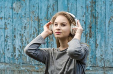 Sevimli kız eski tahta arka plan üzerinde beyaz kablosuz kulaklık müzik dinlemek. Elektronik müzik. Müzik tarzı. Kulağa hoş geliyor. Ses keyfi.