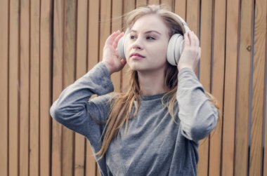 Sevimli kız kahverengi tahta arka plan üzerinde beyaz kablosuz kulaklık müzik dinlemek. Elektronik müzik. Müzik tarzı. Kulağa hoş geliyor. Ses keyfi.