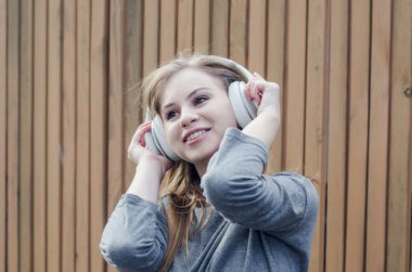 Sevimli kız kahverengi tahta arka plan üzerinde beyaz kablosuz kulaklık müzik dinlemek. Elektronik müzik. Müzik tarzı. Kulağa hoş geliyor. Ses keyfi.
