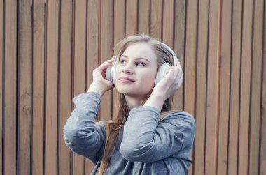 Sevimli kız tahta çit arka plan üzerinde beyaz kablosuz kulaklık müzik dinlemek. Elektronik müzik. Müzik tarzı. Kulağa hoş geliyor. Ses keyfi.