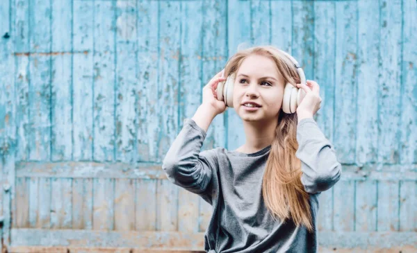 Cute girl listening to music in white wireless headphones on the background of the old board. Electronic music. Musical style. Pleasant sounds. The pleasure of sound.