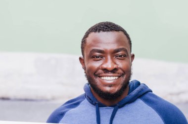 Neşeli pozitif siyah adam yakın bir spor kazaklı bir ışık duvar arka plan portresi. Yarış sorunları. Şehir Fotoğraf, alan. Genç kültür.