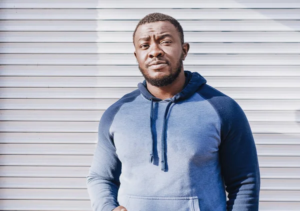 Portrait of a black guy close-up in a sports sweater on the background of a striped bright wall. Cheerful positive person. City photo, space. Youthful culture.