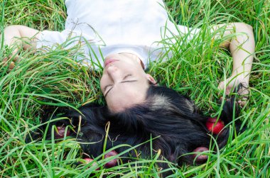 Çekici kız esmer yeşil çimenlerin üzerinde bir glade yatıyor. Saç yere. Kırmızı elma saç. Yaz ruh anılar. Doğal beslenme, sağlık.