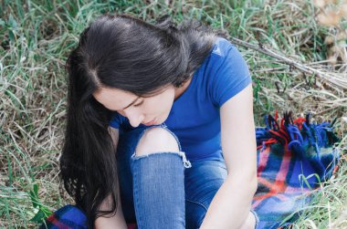 Bahçede bir elma ağacı altında yeşil çimenlerin üzerinde oturan çekici esmer kız. Doğa üzerinde bekletin. Kadın sağlığı. Yaz anıları. Cinsellik, kadınlık