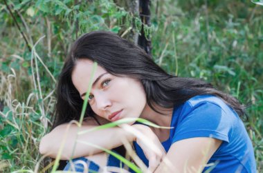 Bahçede bir elma ağacı altında yeşil çimenlerin üzerinde oturan çekici esmer kız. Doğa üzerinde bekletin. Kadın sağlığı. Yaz anıları. Cinsellik, kadınlık