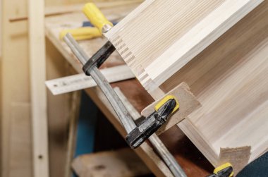 Kelepçeler ile sıkma ahşap kutu yapıştırma. Doğrama atölyesinde çalışmak. Ahşap el sanatları. Tespitleme parçaları.