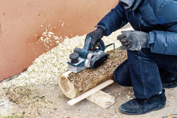 male carpenter grinds a log with hand-held electric planer. Woodwork. Manufacture of wood products. Carpentry workshop