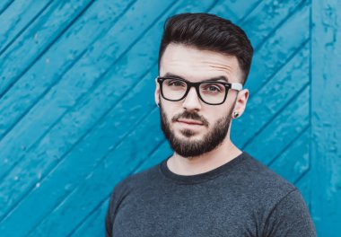 Mavi ahşap arka plan karşı ayakta yakışıklı genç adam portresi. Gençlik Kültür. Berber dükkanı.