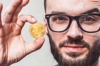 Genç adam portresi. Yüz yakın çekim. Sikke Bitcoin tutar. Cryptocurrency madencilik