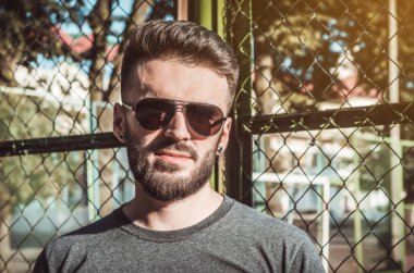 Sakal ve spor alanında, metal ızgara siyah gözlük ile şık genç adam portresi.