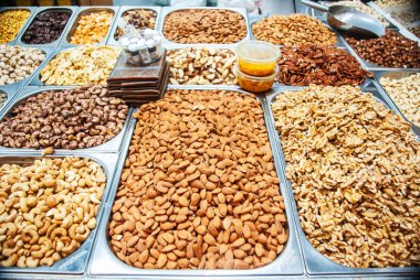 Nuts of various kinds in metal trays on street market clipart