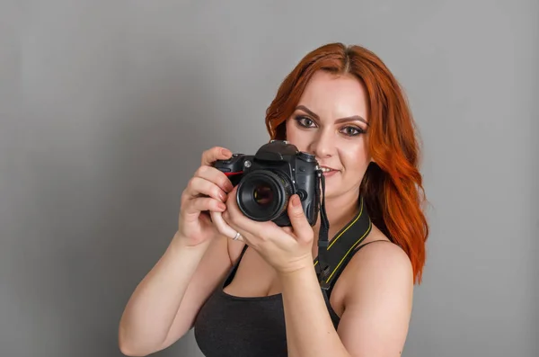 Улыбающаяся Женщина Рыжими Волосами Держит Руках Современную Камеру Серый Фон — стоковое фото