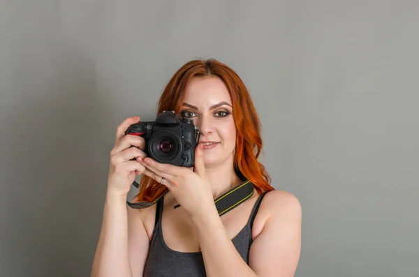 Улыбающаяся Женщина Рыжими Волосами Держит Руках Современную Камеру Серый Фон — стоковое фото