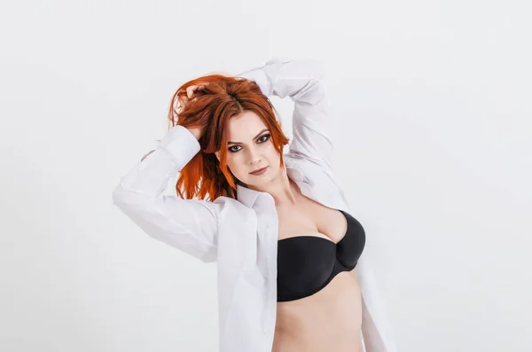 Beautiful woman with red hair in dark bra on the white background, isolated. Sexuality, seduction, exploitation of women, health.