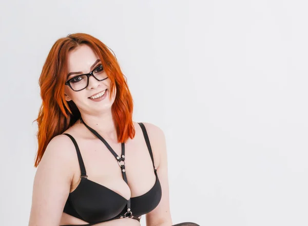 Beautiful woman with red hair in dark bra and glasses on the white background, isolated. Sexuality, seduction, exploitation of women, health.