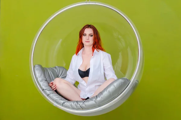 美丽纤细的红头发的白衬衫女人坐在一个圆形透明的挂座位上 在一个浅绿色的背景 妇女健康 — 图库照片
