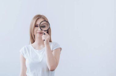 Sarı saçlı kız Büyüteç tutuyor. Genişlemiş göz. Gülümse. Araştırma arama