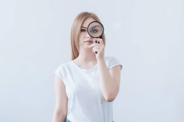 Ragazza con i capelli biondi sta tenendo una lente d'ingrandimento. Occhio allargato. Sorridi. Ricerca di ricerca — Foto Stock