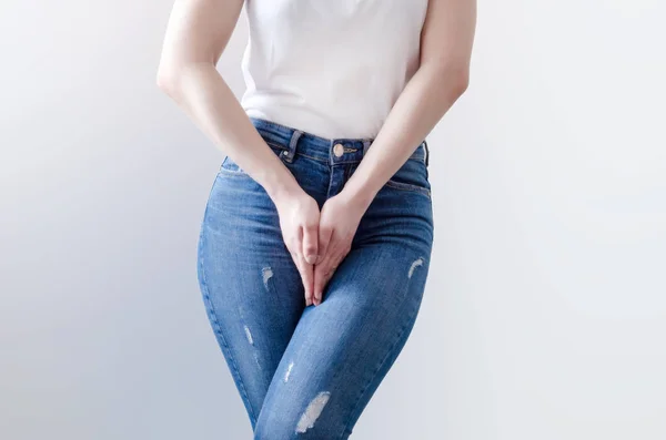 Mujer joven en jeans de pie con las manos entre las piernas —  Fotos de Stock