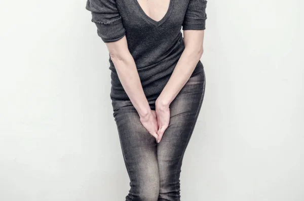 Young slim girl in jeans holds hands pressed between her legs. W — Stok fotoğraf