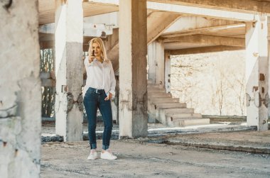 Beyaz tişörtlü bir kadın terk edilmiş bir binada duruyor ve ateş ediyor.