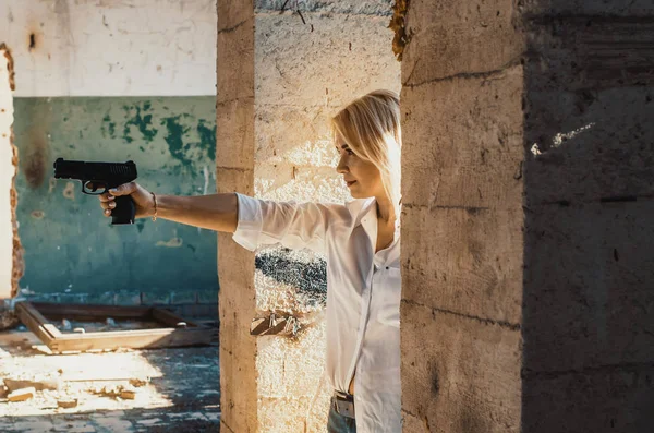 Kvinna i vit skjorta skjuter en pistol i en övergiven byggnad — Stockfoto