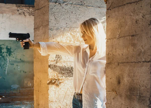 Mujer con camisa blanca dispara una pistola en un edificio abandonado —  Fotos de Stock