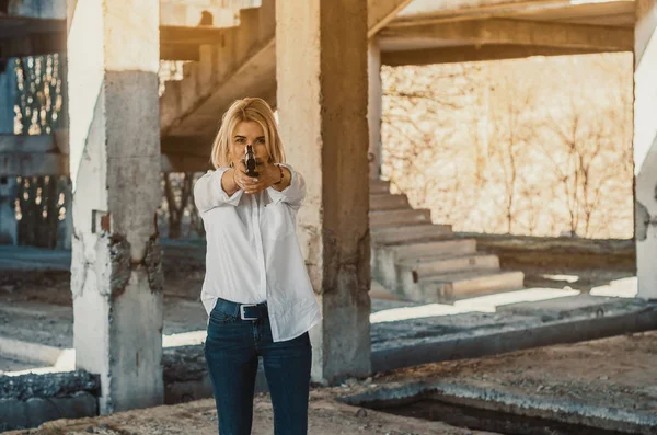 穿着白衬衫的女人站在一座废弃的大楼里，开枪打了一针 — 图库照片