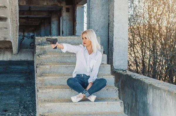 Žena v bílé košili sedí na betonových schodech, střílí z pistole — Stock fotografie