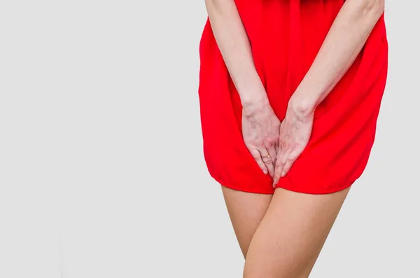 Woman in a red dress holding hands between legs. Experiencing pa — Stock Photo, Image