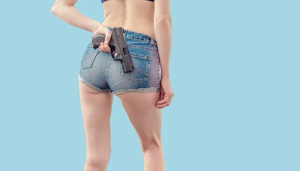 穿着牛仔短裤的年轻女孩在她身后拿着一把黑色手枪 — 图库照片