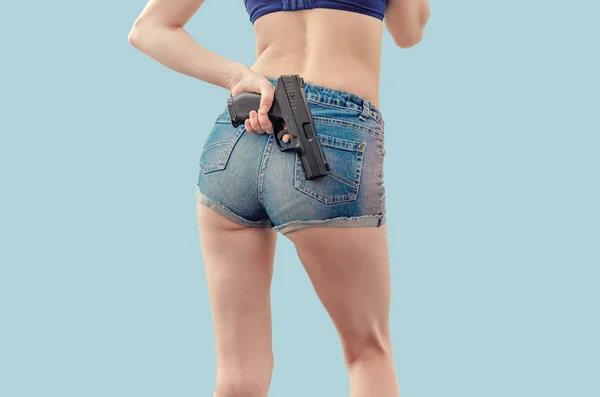 Młoda dziewczyna w szorty dżinsowe trzyma czarny pistolet za nią — Zdjęcie stockowe