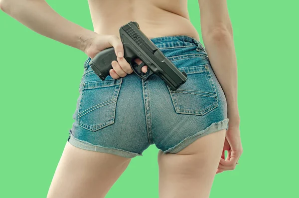 Joven en pantalones cortos de mezclilla está sosteniendo una pistola negra detrás de ella — Foto de Stock