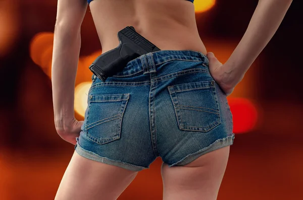 Gadis muda di celana pendek denim memegang pistol hitam terselip ke — Stok Foto
