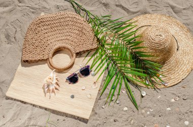 Hasır şapka ve güneş gözlüğü ile palmiye yaprakları kum üzerinde olmak