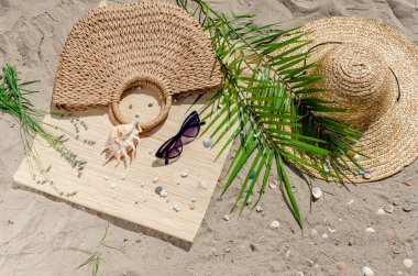 Hasır şapka ve güneş gözlüğü ile palmiye yaprakları kum üzerinde olmak