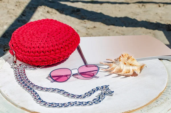 Malá červená ženská kabelka, růžové sluneční brýle, časopis, kohouty — Stock fotografie
