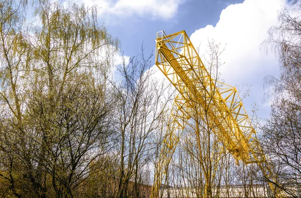 Yellow gantry crane behind the trees on the territory of the ent