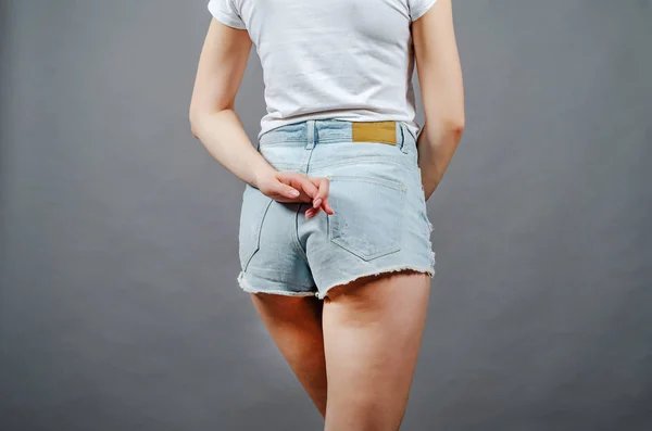 Chica joven en pantalones cortos de mezclilla mantiene los dedos cruzados detrás de ella —  Fotos de Stock