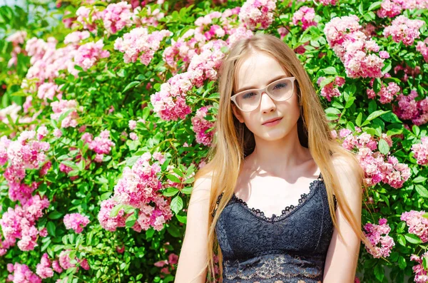Jolie fille dans des lunettes aux cheveux blancs sur un fond de rosier fleuri — Photo
