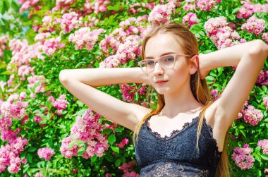 Nice girl in glasses with white hair on a background of a flowering rose bush
