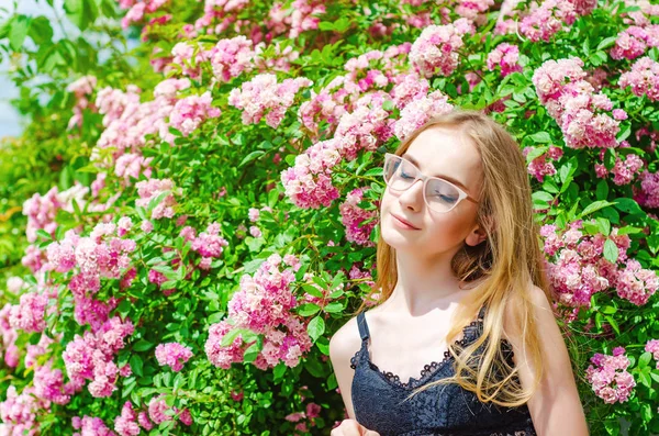 Jolie fille dans des lunettes aux cheveux blancs sur un fond de rosier fleuri — Photo