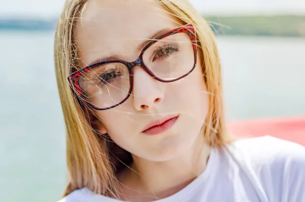 Sommerporträt eines blonden Mädchens mit Brille auf einem See-Hintergrund — Stockfoto