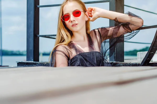 Adolescente loira em óculos de sol vermelhos posando em preto metal stai — Fotografia de Stock