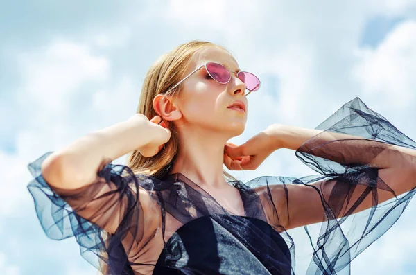 Chica joven en gafas de sol rojas posando sobre el fondo del cielo, brillante — Foto de Stock