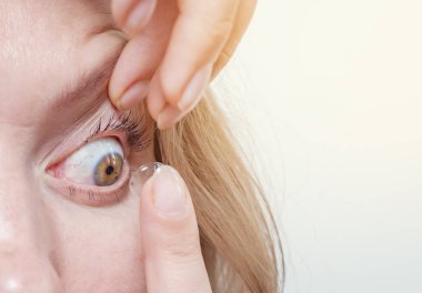 Woman inserts a contact lens into the eye. clipart