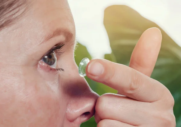 Woman inserts a contact lens into the eye.