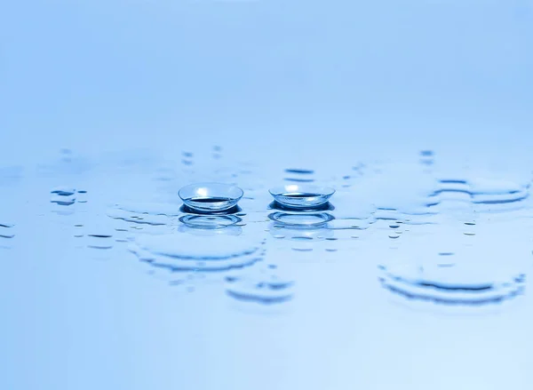 Lentes de contacto para los ojos en el vidrio entre las gotas de agua en azul. Equipo óptico, buena visión, optometrista . — Foto de Stock